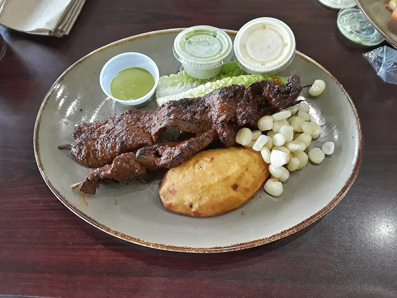 Anticuchos a la parrilla con papa dorada, choclo y cremas de ají
