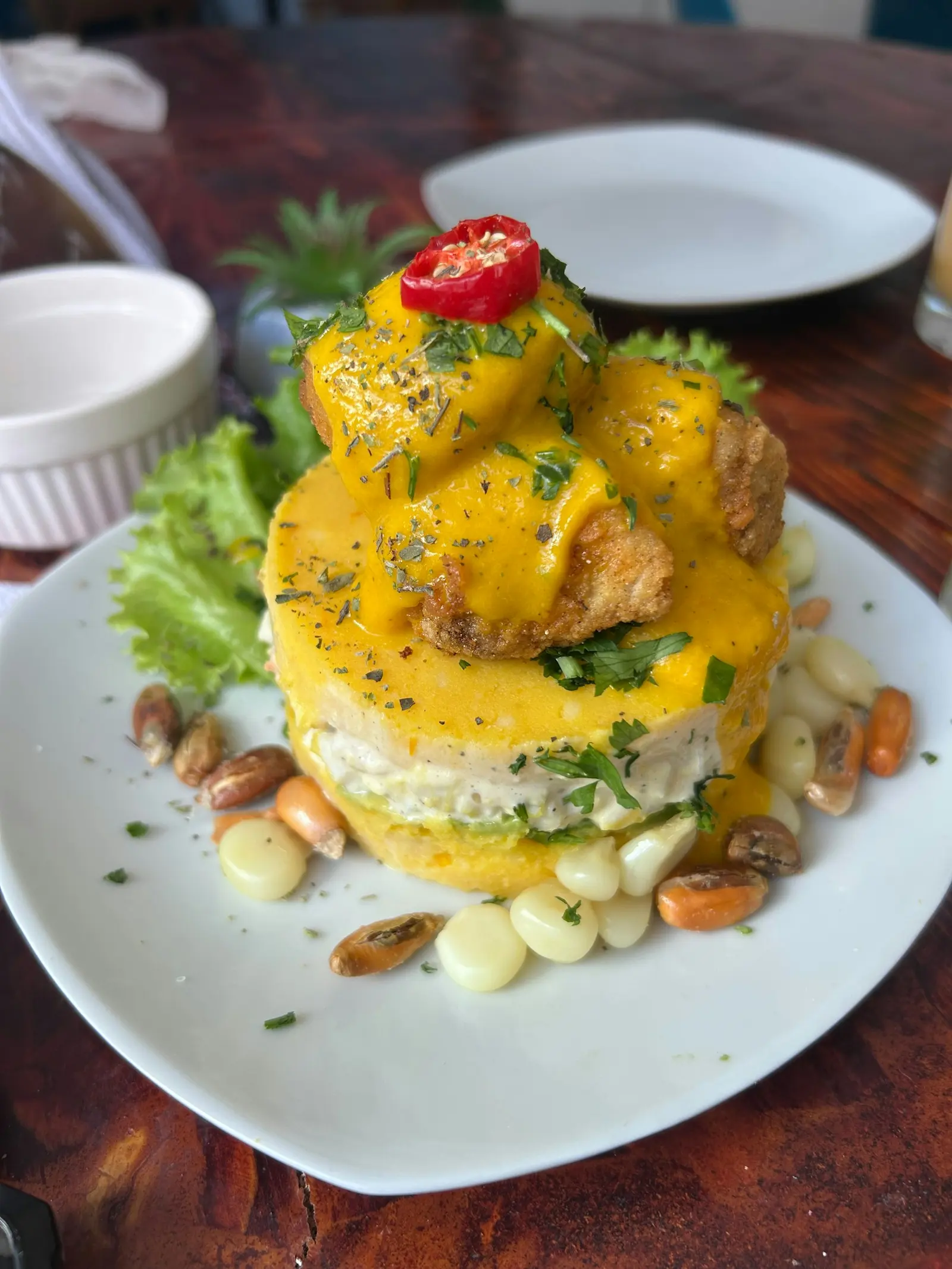 Causa rellena bañada en crema de ají amarillo, decorada con rocoto y acompañada de choclo y cancha